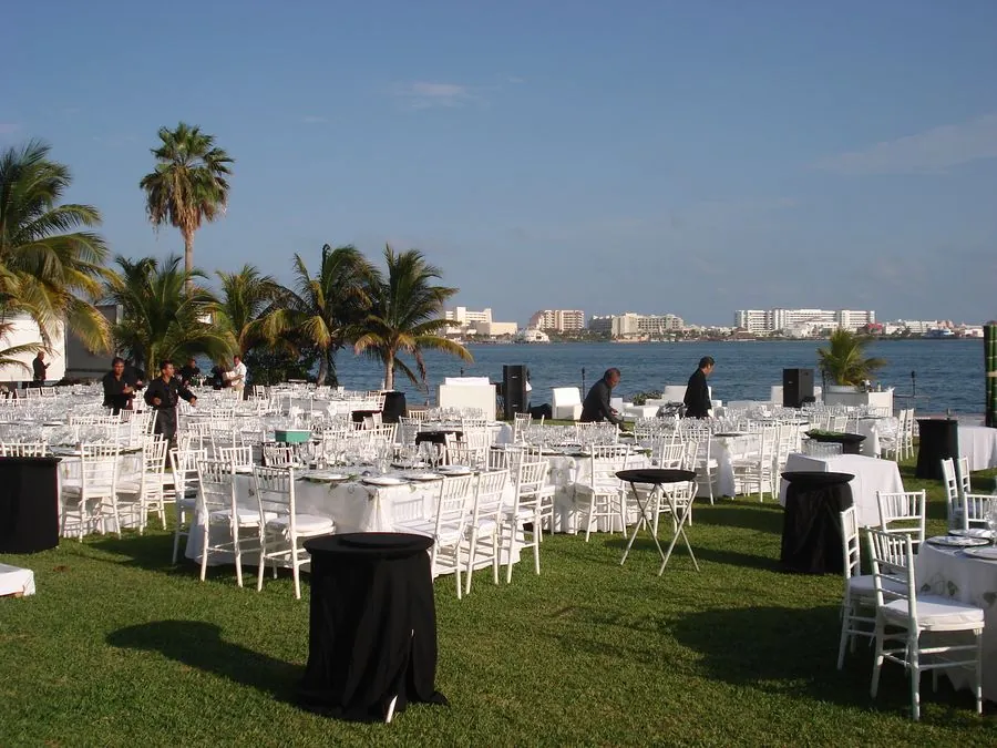Montaje en jardín frente al mar con sillas blancas y mesas coctel negras