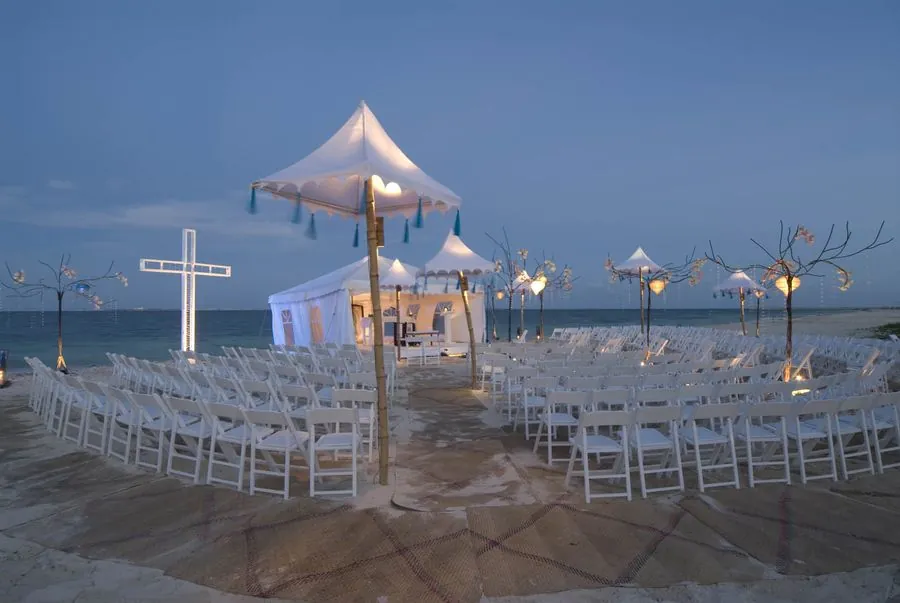 Ceremonia en la playa al atardecer con sillas blancas y faroles