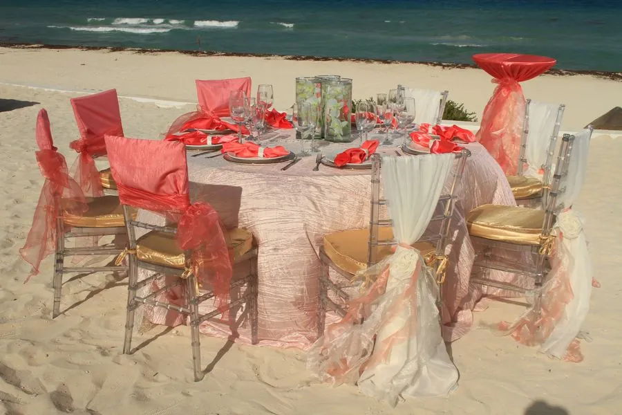 Mesa en la playa con mantelería rosa y sillas Tiffany