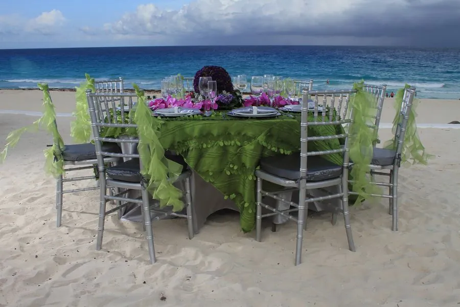 Mesa en la playa con mantel verde texturizado y sillas Tiffany plata