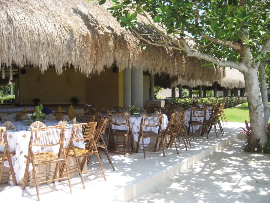 Montaje bajo palapa con sillas de madera y vista al mar