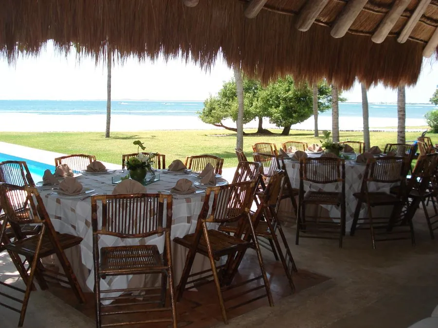Mesas redondas bajo palapa con sillas plegables de madera