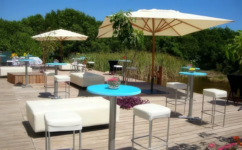 Sala lounge blanca y mesas periqueras turquesa con bancos altos bajo sombrillas en una terraza